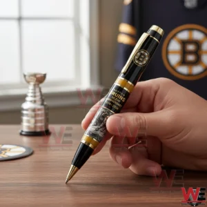 Boston Bruins 102nd Anniversary Commemorative Pen 3 Hand holding a black and gold Boston Bruins anniversary pen with 102nd Anniversary 1924 2026 text in a hockey themed room.