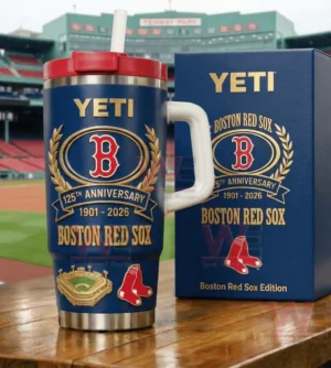 Blue Boston Red Sox anniversary Yeti tumbler with straw and handle next to a matching blue box at a baseball stadium setting.