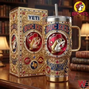 Ornate gold Buc Ees tumbler with beaver emblem standing beside its decorative box on a wooden table!