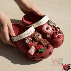 Buc Ee's Valentine Clogs Crocs with Charms 4 Hands holding red Buc Ees clogs with white straps covered in Valentine themed charms including a donut roses chocolate and heart shaped sunglasses!