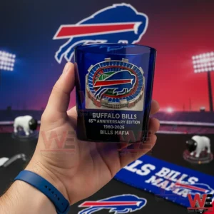 Hand holding a blue Buffalo Bills sixty fifth anniversary whiskey glass with stadium logo against a football themed backdrop!