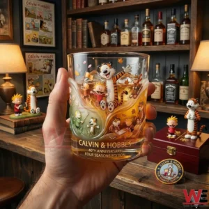A hand holding a Calvin and Hobbes anniversary whiskey glass decorated with four seasonal illustrations displayed in a warm indoor environment!