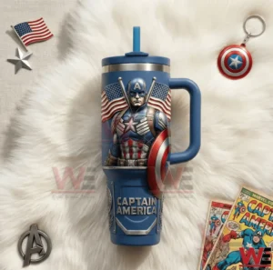 A blue insulated tumbler with handle and straw decorated with a patriotic superhero shield figure and American flag motifs placed on a white fur background!