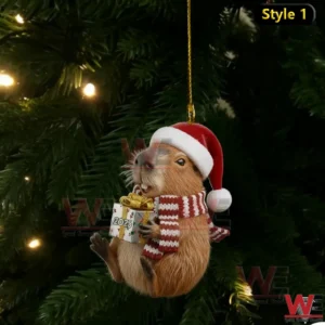A capybara ornament in a Santa hat and striped scarf holding a 2025 gift while hanging on a Christmas tree branch with warm lights!