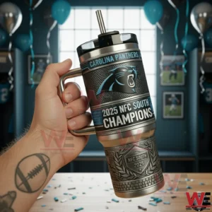 Hand holding a Carolina Panthers themed stainless steel tumbler with handle and straw showing 2025 NFC South Champions text in a decorated room with balloons and framed football photos!