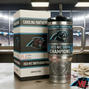Carolina Panthers 2025 NFC South Champions Limited Edition Tumbler 4 Carolina Panthers 2025 NFC South Champions stainless steel tumbler with handle and straw placed next to a matching limited edition gift box on a tabletop with a blurred stadium background!