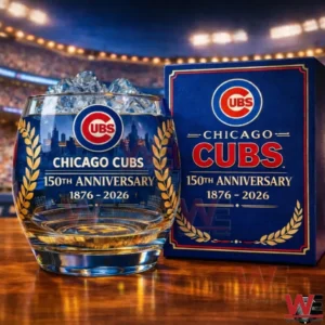 Chicago Cubs Commemorative 150th Anniversary Whiskey Glass 3 Chicago Cubs one hundred fiftieth anniversary whiskey glass with ice on a wooden table beside a blue commemorative box with stadium lights in the background.