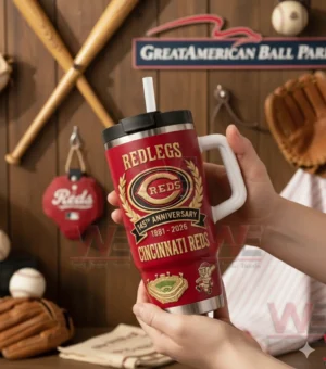 Hands holding a red Cincinnati Reds Redlegs tumbler with white handle and straw showing 145th anniversary 1881 2026 Cincinnati Reds design with bats and gloves in the background