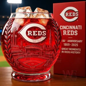 Red Cincinnati Reds whiskey glass with ice and etched stadium design next to an anniversary gift box on a table in a stadium background.