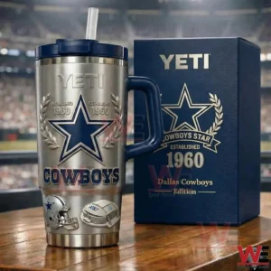 Stainless Dallas Cowboys tumbler with blue handle and straw next to a matching navy gift box featuring the Cowboys star established 1960 design in a stadium background