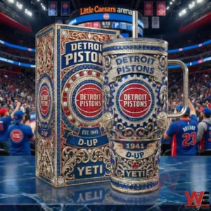 A Detroit Pistons themed insulated tumbler with intricate patterns and team branding stands beside its matching box on a reflective surface in a professional basketball stadium!