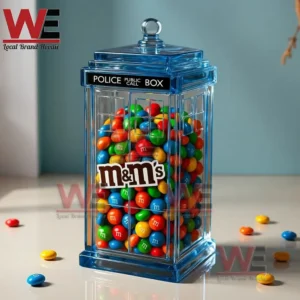 Doctor Who Police Box M&M Candy Jar 3 Blue police box candy jar full of colorful chocolate candies on a reflective table with scattered candies nearby.