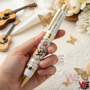 Hand holding a white and gold Dolly Parton eightieth anniversary ballpoint pen with butterfly accents and a guitar illustration against a soft decorative background.