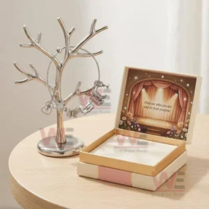 Dolly Parton Adjustable Charm Bracelet 3 Silver charm bracelet on a jewelry tree stand beside an open pastel gift box featuring a stage illustration and an inspirational message.