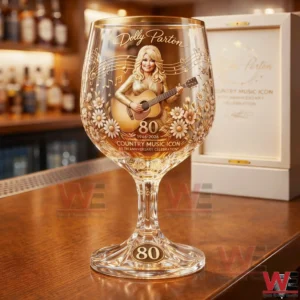 A clear decorative wine glass on a bar counter featuring Dolly Parton with a guitar musical notes floral details and an 80 year country music icon celebration design!