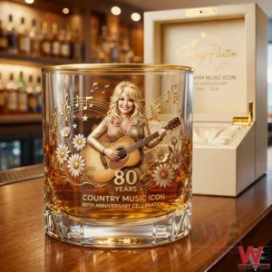 Whiskey glass with a golden Dolly Parton illustration celebrating eighty years of a country music legend placed on a wooden bar with a gift box behind it!