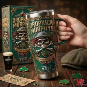 An insulated tumbler with a green and gold Irish themed design featuring a skull clover and Dropkick Murphys branding displayed on a wooden table with matching decorative elements!