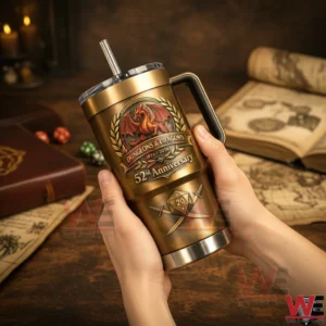 Hands holding a bronze Dungeons And Dragons 52nd anniversary tumbler with handle and straw showing a dragon crest laurel wreath and twenty sided dice emblem on a fantasy themed table