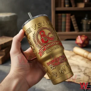 Hand holding a gold and red Dungeons and Dragons anniversary tumbler with dragon crest and anniversary dates in front of books and tabletop gaming props!