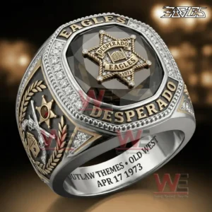 Close up view of a silver and gold western themed ring with a large black gemstone centerpiece and a star badge emblem reading Desperado Eagles 1973 surrounded by sparkling stones and engraved text!