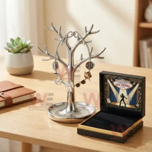 Adjustable charm bracelet on a jewelry tree stand with music icons and a Las Vegas live charm beside an open gift box on a wooden desk.