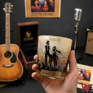 A hand holding a Fleetwood Mac Rumours whiskey glass surrounded by musical instruments and classic band decor!