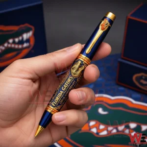 Florida Gators 120th Anniversary 1906-2026 Pen 3 Hand holding a navy and gold Florida Gators commemorative ballpoint pen with ornate gold details alligator artwork and anniversary text against a Florida Gators themed background.