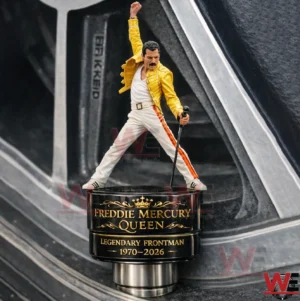 Miniature Freddie Mercury figure in a yellow jacket standing on a black and gold tire valve cap base labeled Freddie Mercury Queen Legendary Frontman 1970 2026 with a tire wheel background.