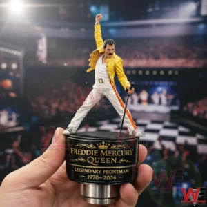 Freddie Mercury Legendary Frontman 1970-2026 Tire Valve Caps 3 Hand holding a tire valve cap with a miniature Freddie Mercury figure in a yellow jacket on a black and gold base reading Freddie Mercury Queen Legendary Frontman 1970 2026 with a concert stage background.