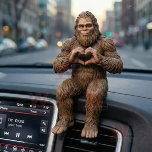 Bigfoot figurine with brown fur sitting on a car dashboard and forming a heart shape with its hands with a blurred city street background!