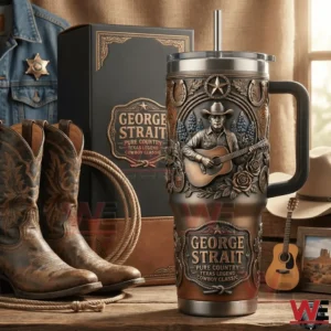 Handled tumbler with embossed cowboy playing guitar and western floral details beside a matching George Strait gift box with cowboy boots and rope on a wooden table!