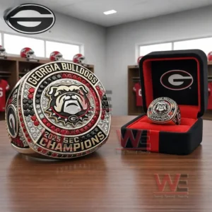 Georgia Bulldogs 2025 SEC Champions ring with a bulldog emblem and red black and clear stones displayed next to a black and red presentation box in a locker room setting!