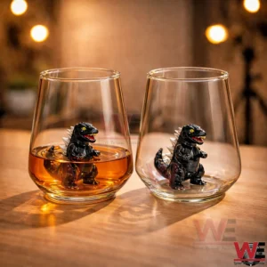 A pair of transparent glasses on a table each holding a tiny black monster figurine with one glass partially filled with brown liquid!