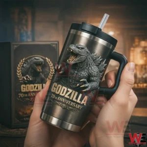 Hands holding a dark stainless Godzilla tumbler with handle and straw showing a roaring Godzilla graphic and 70th anniversary text with a matching collector edition gift box behind