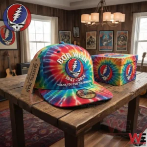 Tie dye style cap with skull emblem resting on a wooden table in a cozy music room filled with guitars and artwork!