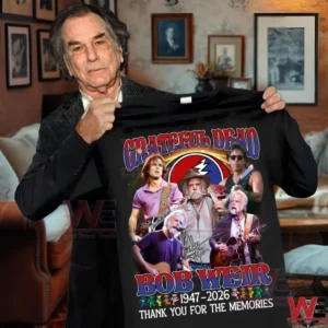 Man holding a black music shirt with colorful guitarist artwork inside a cozy room setting!