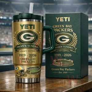 Metallic gold insulated tumbler with dark green handle and straw featuring Green Bay Packers frozen tundra legacy edition graphics beside a matching green collector box on a wooden table with a stadium background!