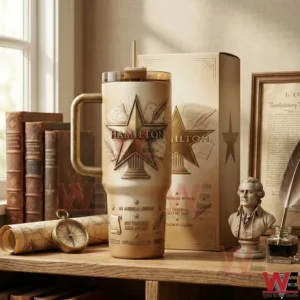 Hamilton themed tumbler with gold star emblem handle clear lid and straw displayed on a desk with books and historical decor!
