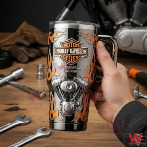 Hand holding a Harley Davidson insulated tumbler with orange flames and engine design with garage tools and motorcycle parts in the background!