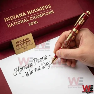 A hand holding a red and gold Indiana Hoosiers championship pen while writing on paper with a branded collector box displayed nearby!
