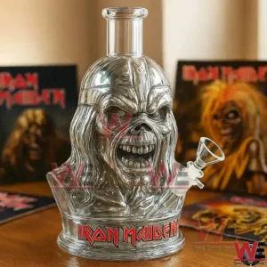 Clear glass skull shaped water pipe with Iron Maiden logo on the base displayed in front of Iron Maiden album covers.