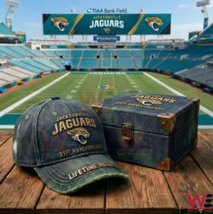 A Jacksonville Jaguars anniversary cap and matching keepsake box displayed on a wooden table with a football field and stadium seating in the background!