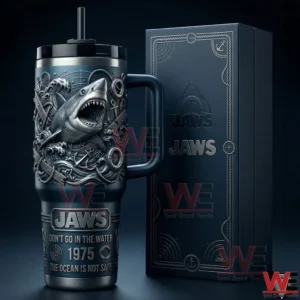 Blue handled tumbler with embossed shark and ocean themed details beside a matching Jaws gift box on a dark studio background!