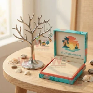Silver adjustable charm bracelet with tropical cocktail parrot island flip flops guitar and compass charms hanging on a jewelry tree stand next to an open sunset themed gift box.