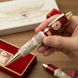 Hand holding a red and gold Kansas City Chiefs commemorative pen with detailed engraved artwork beside a red branded gift box on a wooden table!