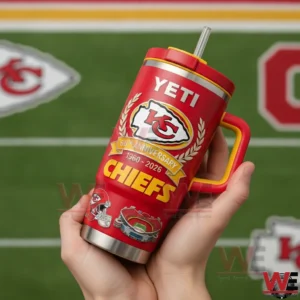 Hands holding a red Kansas City Chiefs tumbler with handle and straw showing the arrowhead logo laurel wreath and 66th anniversary 1960 2026 Chiefs design on a football field background