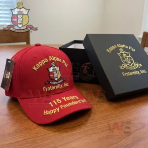 Red Kappa Alpha Psi Fraternity Inc cap with embroidered crest gold lettering and 115 years Happy Founders Day text displayed on a table beside a branded black gift box!