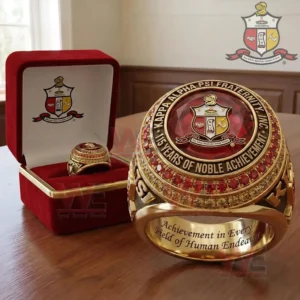 Gold Kappa Alpha Psi fraternity ring with large red gemstone crest centerpiece engraved anniversary text red stone accents and an open red velvet presentation box with matching ring inside!