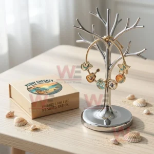 Gold tone adjustable charm bracelet on a jewelry tree with hat guitar palm tree compass sunset and star music note charms beside a Kenny Chesney gift box and seashells.