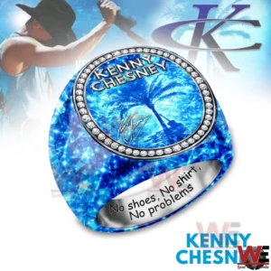 A blue faceted gemstone style ring with an oval face reading KENNY CHESNEY above a palm tree beach scene surrounded by diamond like stones with an engraved interior message and a faded concert background!